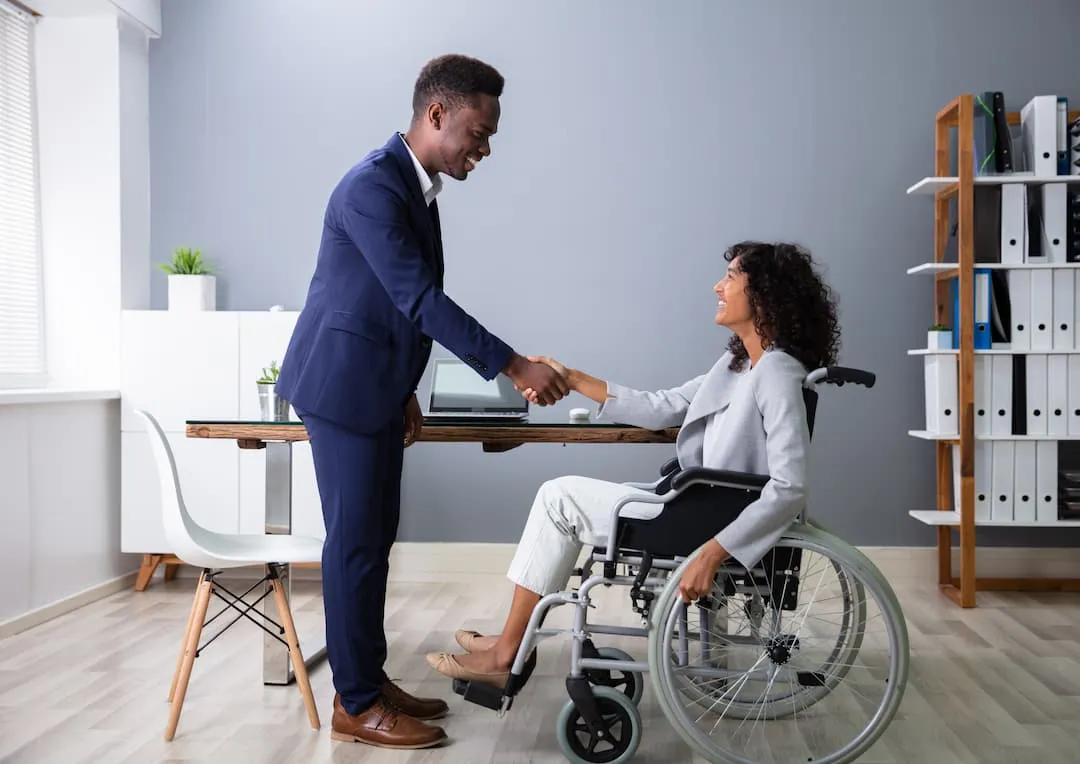 A woman in a wheelchair shaking hands with an adviser across a desk